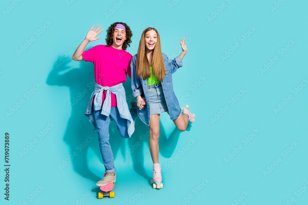 Full body photo of carefree teenagers like sports riding skateboard and rollerskates raised arms up isolated on aquamarine color background Full body photo of carefree teenagers like sports riding skateboard and rollerskates raised arms up isolated on aquamarine color background