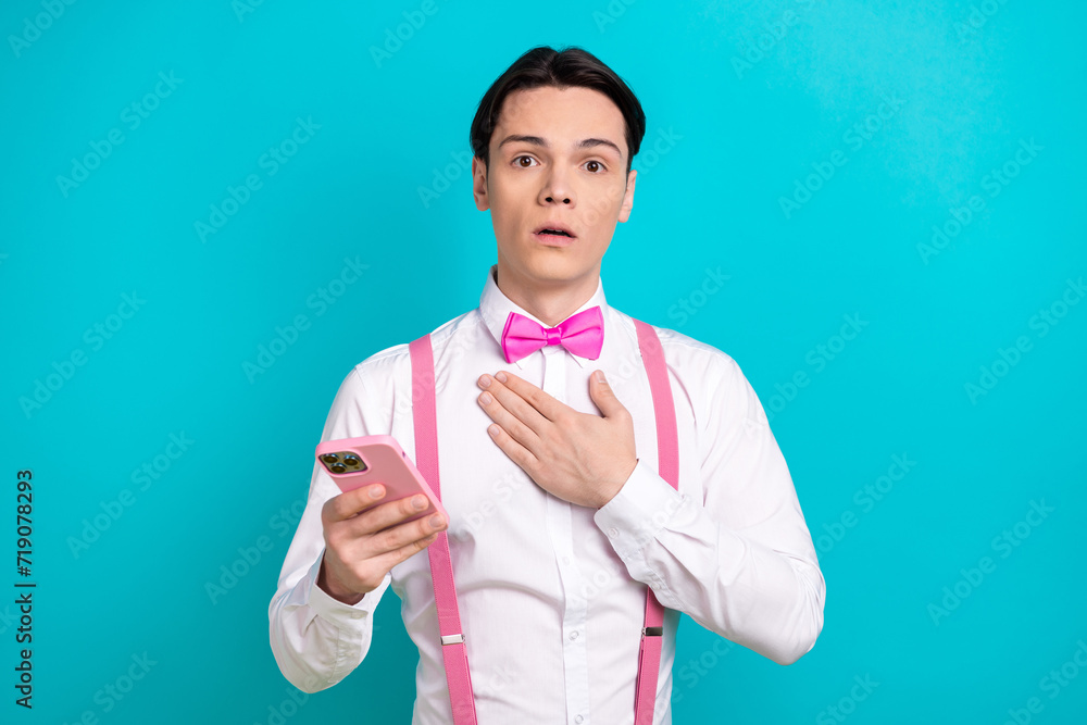 Photo portrait of pretty young male touch chest frightened hold device wear trendy pink outfit isolated on cyan color background Photo portrait of pretty young male touch chest frightened hold device wear trendy pink outfit isolated on cyan color background