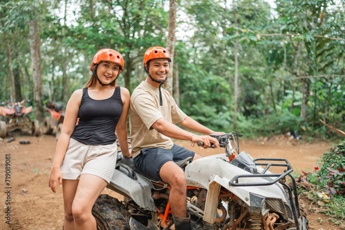 happy asian couple smiling and looking at the camera while sitting on atv together at tracking area