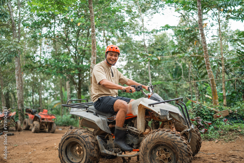 Obraz premium happy asian man looking at the camera while riding the atv at atv arena