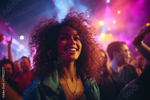 Charming curly young woman in a blue jeans jacket having fun in a nightclub under neon lights among dancing people