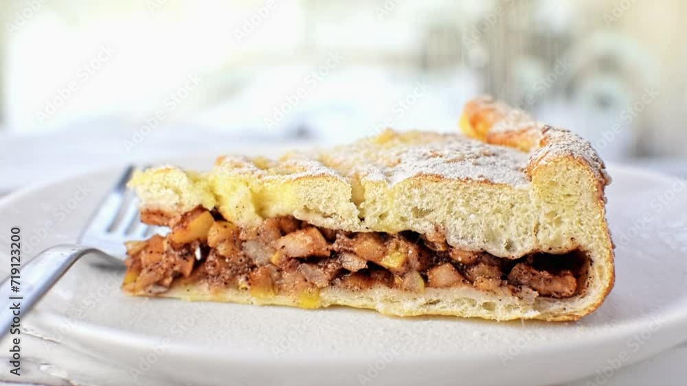 A piece of cinnamon apple pie sprinkle powdered sugar on top. Delicious dessert, fruit cake on a white plate with fork on table. A piece of cinnamon apple pie sprinkle powdered sugar on top. Delicious dessert, fruit cake on a white plate with fork on table.