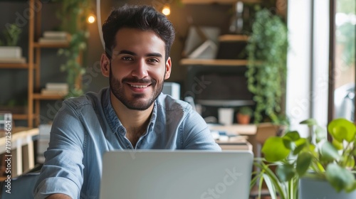 Modern Office: Portrait of Stylish Hispanic Businessman Works on Laptop, Does Data Analysis and Creative Designer, Looks at Camera and Smiles. Digital Entrepreneur Works on e-Commerce Startup Project 