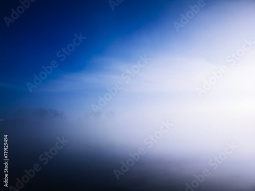 winter foggy morning by the lake, minimal landscape, blue and white, trees emerging from the fog in the distance, abstract landscape