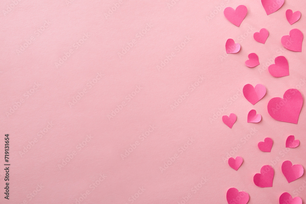 Love background with fuxia pink heart cutouts of various sizes on the right edge isolated on a pink background