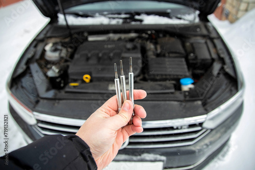 Modern ceramic glow plugs in hand against the background of a diesel car engine in winter in cold weather. Breakdown and replacement of glow plug, close-up photo