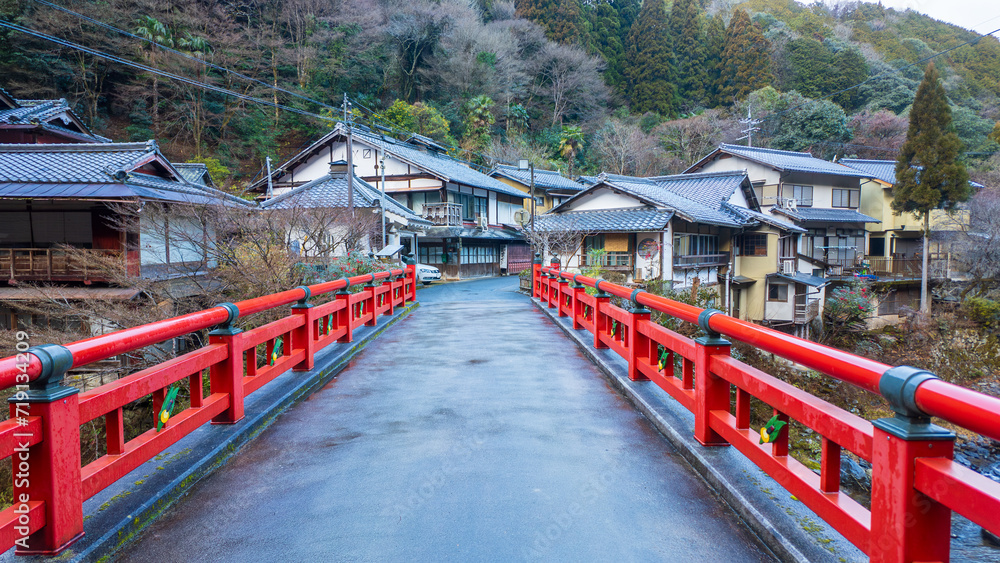 Narrow red bridge leads to traditional houses in Japanese village