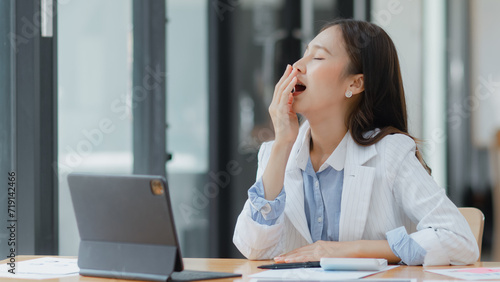 Asian businesswoman working on tablet with documents and stressed over worked from work in the office, Tired and Overworked businesswoman concept.
