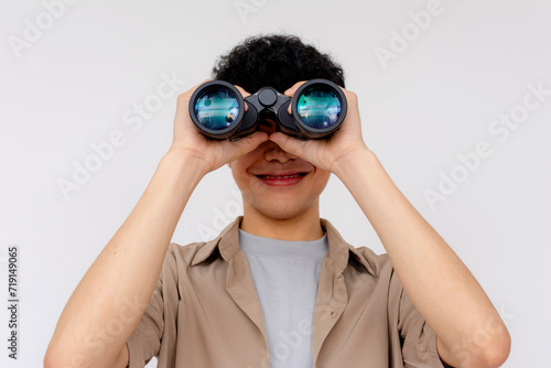 A cheerful young Asian man is using binoculars to explore, symbolizing curiosity, search, and discovery.
