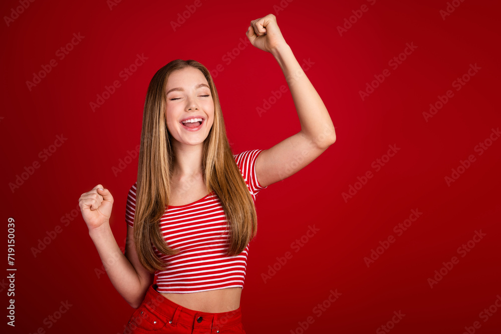 Portrait of ecstatic teenager with long hair wear striped t-shirt raising fists scream yeah win lottery isolated on red color background Portrait of ecstatic teenager with long hair wear striped t-shirt raising fists scream yeah win lottery isolated on red color background