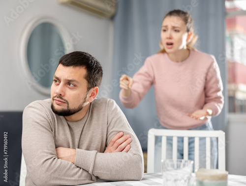 Young adult couple quarreling at home  woman sitting at table and ignoring arguing man