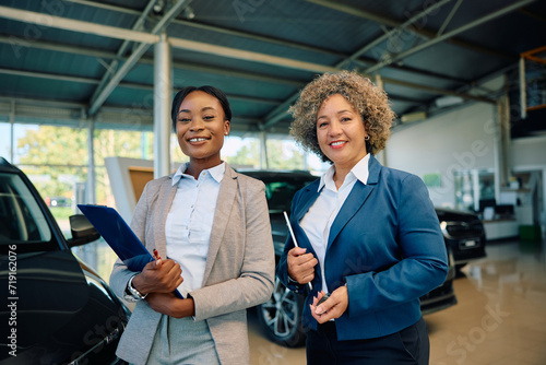 Happy black saleswomen at car dealership looking at camera. photo