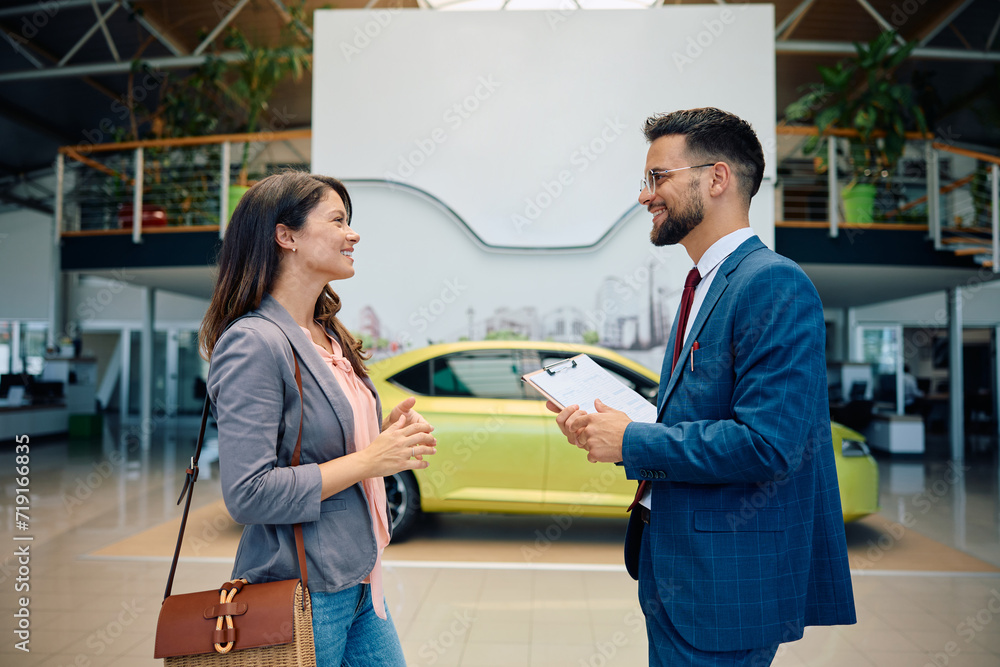 Fototapeta premium Happy salesman and his female customer talking at car dealership.