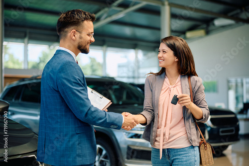 Happy woman and car salesman shaking hands in showroom.