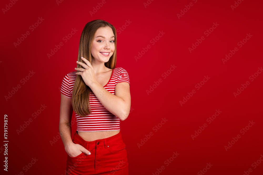Photo of sweet shiny girl wear striped top taking care hairdo empty space isolated red color background Photo of sweet shiny girl wear striped top taking care hairdo empty space isolated red color background