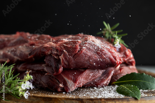 Food Composition Neck part of reindeer meat on a wooden chopping board in close-up. Salt is pouring out photo