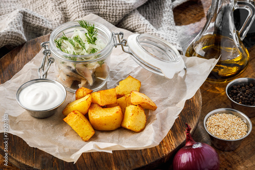 Potato wedges with herring with onions in a jar sour cream on a wooden board