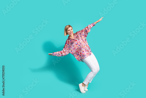 Full size photo of overjoyed adorable girl wear oversize shirt white trousers standing on tiptoes isolated on turquoise color background