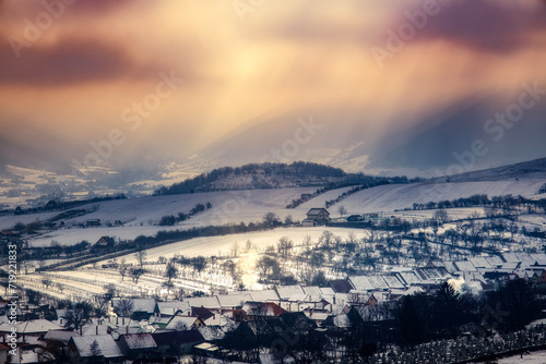 the rays of the sun among the clouds on the the village covered in snow, Orlat village, Sibiu county, Romania