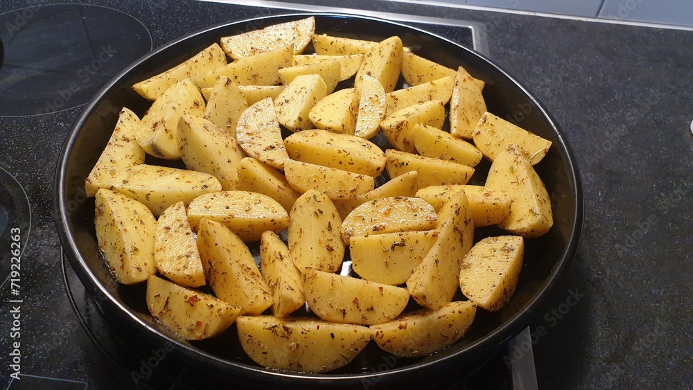 Sliced raw potatoes are mixed with seasonings are placed in a black tray, Roasted potatoes Menu. Sliced raw potatoes are mixed with seasonings are placed in a black tray, Roasted potatoes Menu.