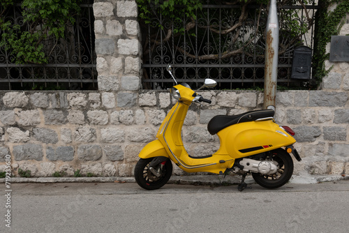 Kotor, Montenegro - 06 17 2023: A yellow scooter parked against the stone wall at Dobrota's promenade  © Sara