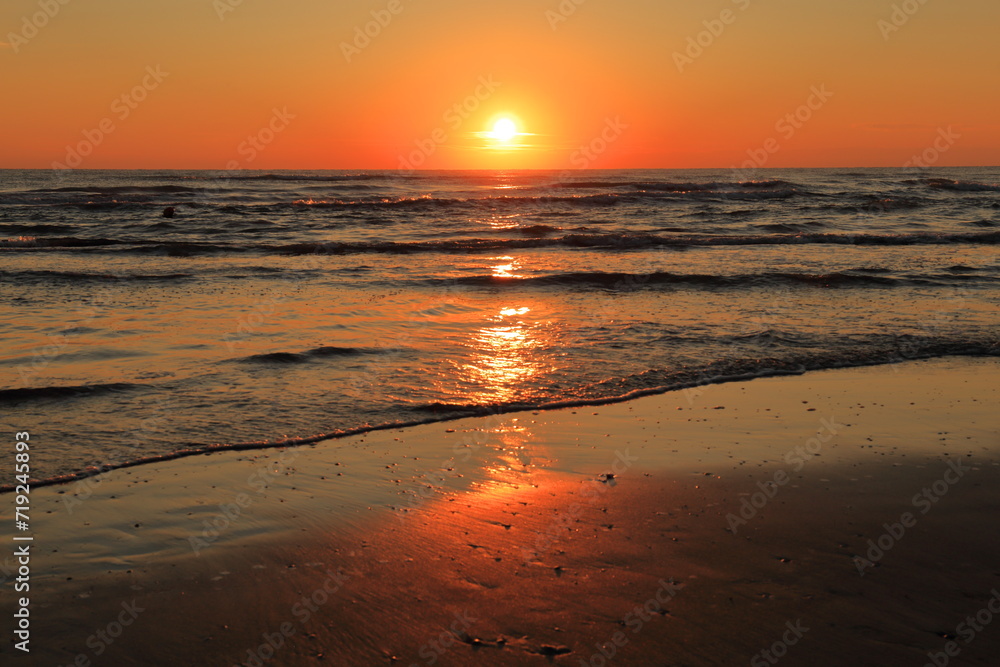 Sole che nasce a Riccione dal mare adriatico con raggio di sole sulla battigia