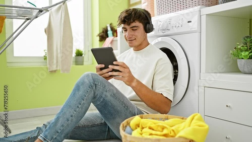 Happy hispanic teen jammin' to tunes on touchpad while waiting for laundry cycle in cozy home's laundry room photo