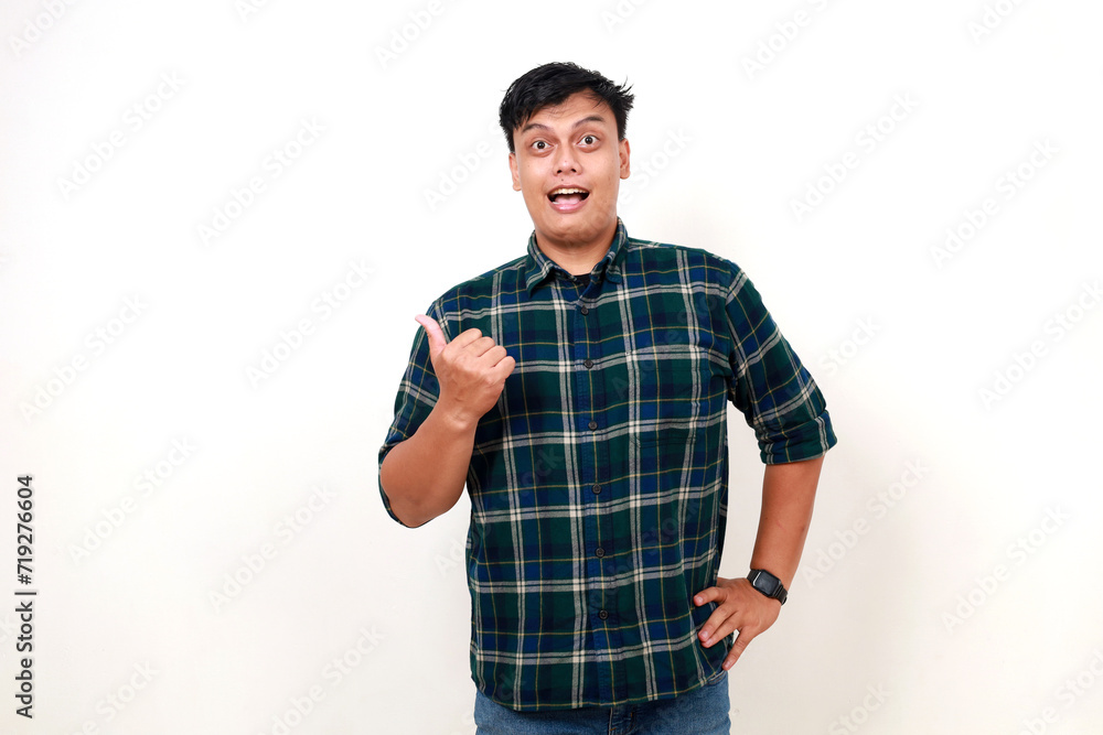 Wow excited expression of young asian man standing while pointing sideways on empty space Wow excited expression of young asian man standing while pointing sideways on empty space