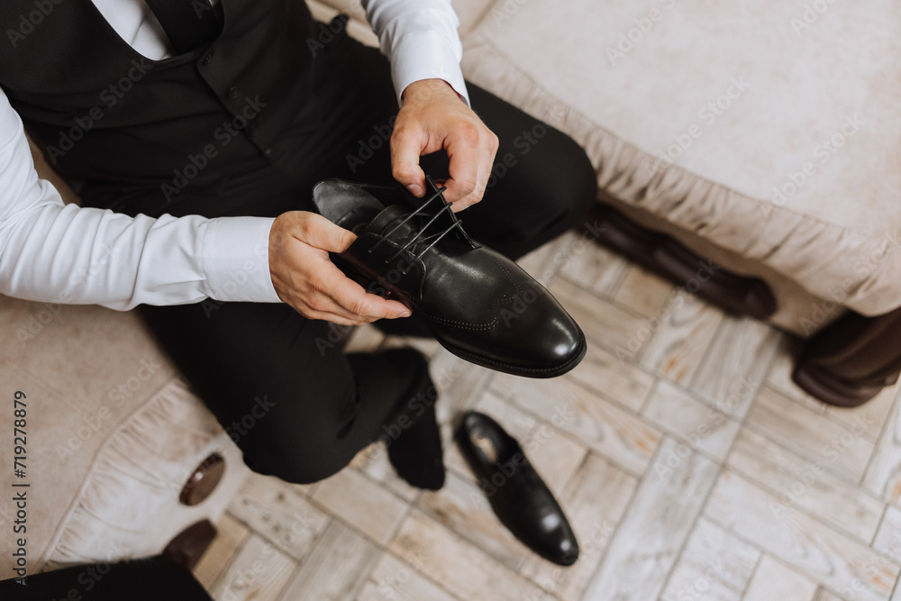Fototapeta premium A young man put on black leather boots indoors. Close-up photo. Detail of a groom putting on his shoes