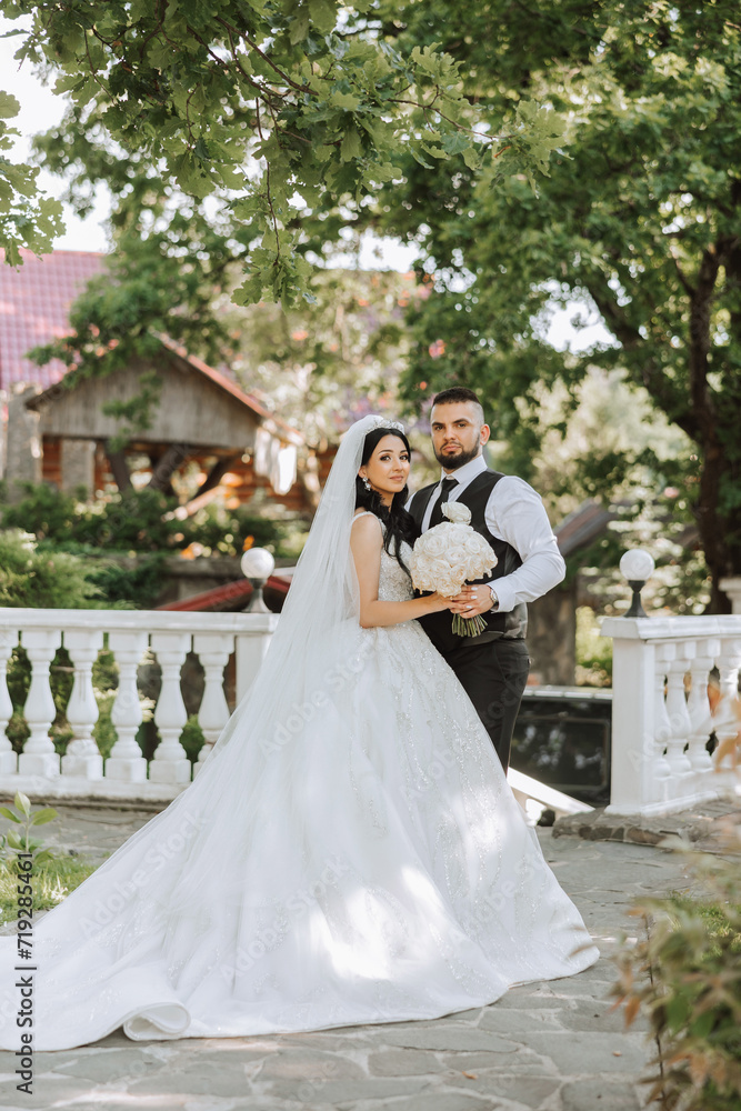 A handsome groom embraces his bride in a lush white dress and smiles in a beautiful outdoor setting. Under the open sky. High quality photo. A newlywed couple poses together on a sunny summer day. A handsome groom embraces his bride in a lush white dress and smiles in a beautiful outdoor setting. Under the open sky. High quality photo. A newlywed couple poses together on a sunny summer day.