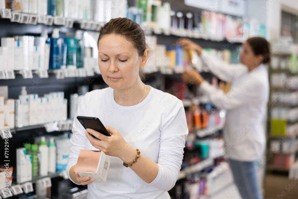 Positive woman customer using phone to search information about selected product at pharmacy