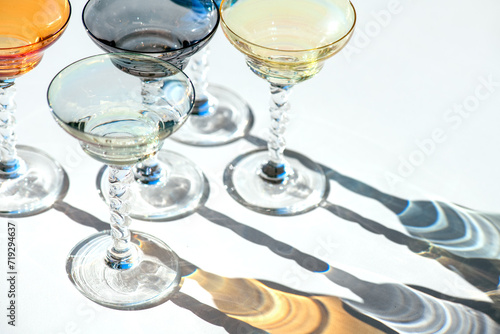 Crystal colorful stemware set with reflection over white background. Colourful elite set of empty alcohol liquor glasses on white, border design. Stemmed glasses, drinkware