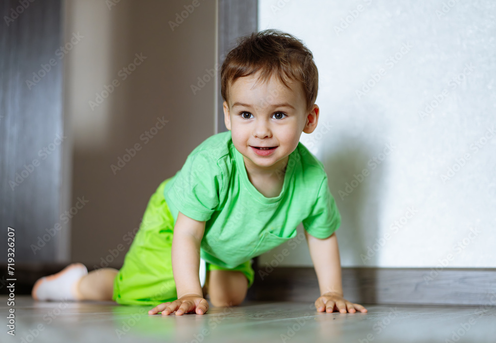 Little boy crawls on the floor in green T-shirt and shorts