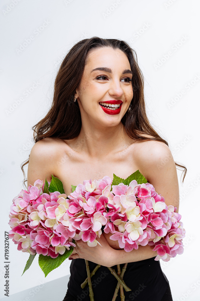 Beautiful young woman with bright makeup and red lips holds pink hydrangea flowers in her hands on white background Beautiful young woman with bright makeup and red lips holds pink hydrangea flowers in her hands on white background
