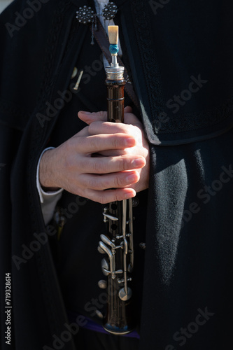 Un hombre con capa castellana negra sostiene entre sus manos una dulzaina o flauta dulce. photo
