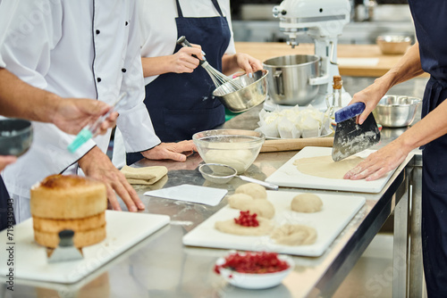 cropped view of hard working chefs and chief cook working with dough on kitchen, confectionery photo