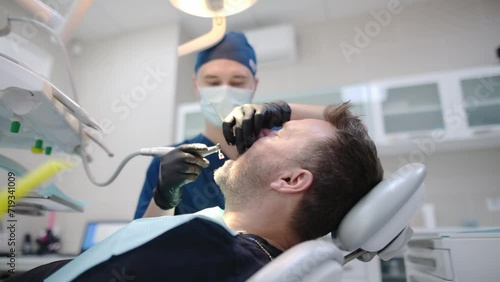Dentist and patient in the medical center. The doctor makes a professional oral hygiene for the teeth of a mature man using dental tools. Deep teeth cleaning procedure by a dental hygienist photo