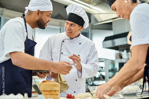 cheerful mature chief cook in white hat explaining information joyfully to his multiracial chefs
