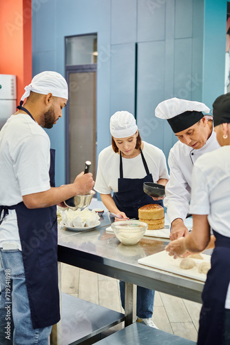 multicultural team of chefs in aprons and toques working on pastry together with chief cook
