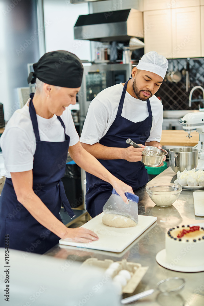 focus on young african american chef in toque whisking next to his blurred jolly mature colleague focus on young african american chef in toque whisking next to his blurred jolly mature colleague