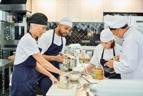 good looking chefs in aprons and toques working together with chief cook on pastry, confectionery © LIGHTFIELD STUDIOS