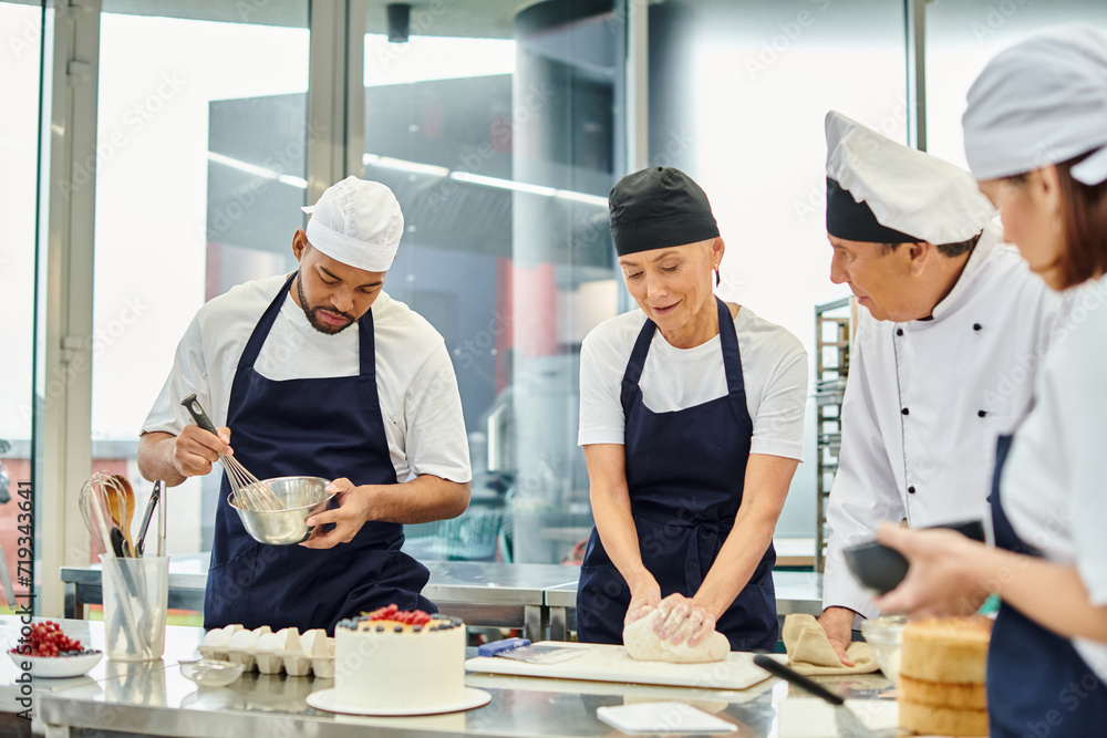 jolly mature woman in toque working with dough next to her diverse colleagues and chief cook jolly mature woman in toque working with dough next to her diverse colleagues and chief cook