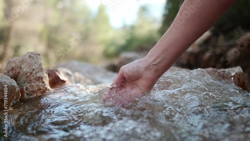 Mature woman touching and scooping up the purest transparent water in a mountain river flowing among the stones. Details of a sunny day in the mountains. Pure clean water in a mountain river