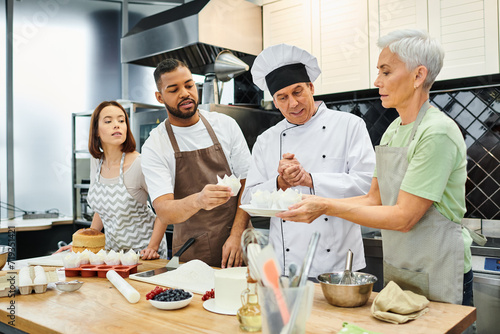 good looking interracial people in aprons listening to mature cheerful chef during cooking lesson