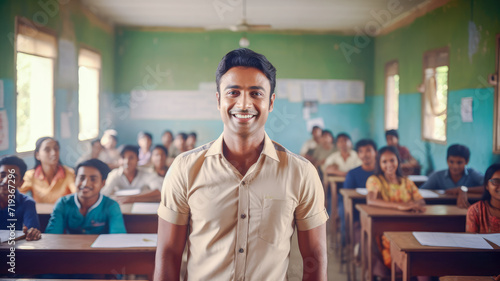 cadid shot of smiling male teacher in a class at elementary school looking at camera with learning smiling students on background