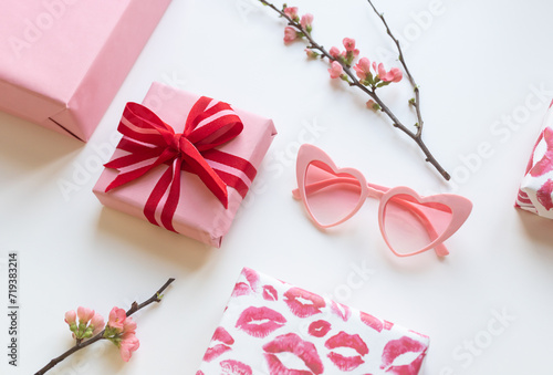 Gift boxes with red bow, lipstick kisses and quince flowers with heart shaped sunglasses on the white background. Valentine's day concept card. © mariarom
