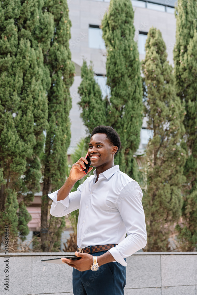 Confident black Businessman Talking on Phone While Holding Tablet Outdoors Confident black Businessman Talking on Phone While Holding Tablet Outdoors
