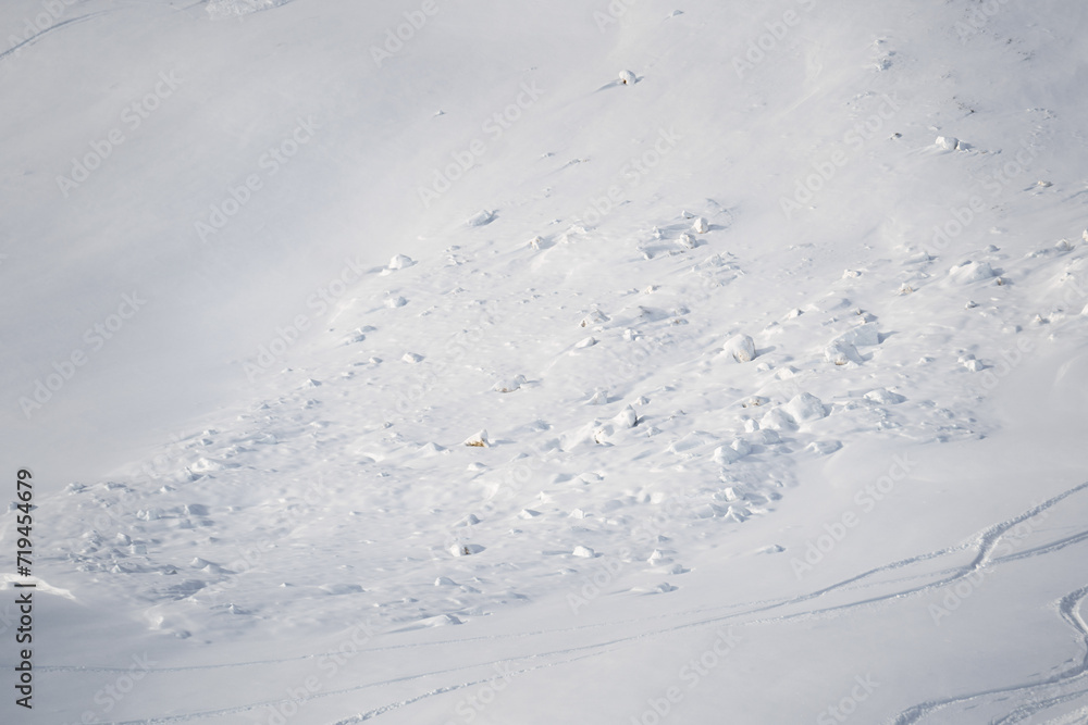 Winterliche Alpen, Überreste eines Lawinenabgangs. Schneetrümmer verteilen sich über das Berggelände und zeigen die Kraft der Lawine auf den schneebedeckten Hängen