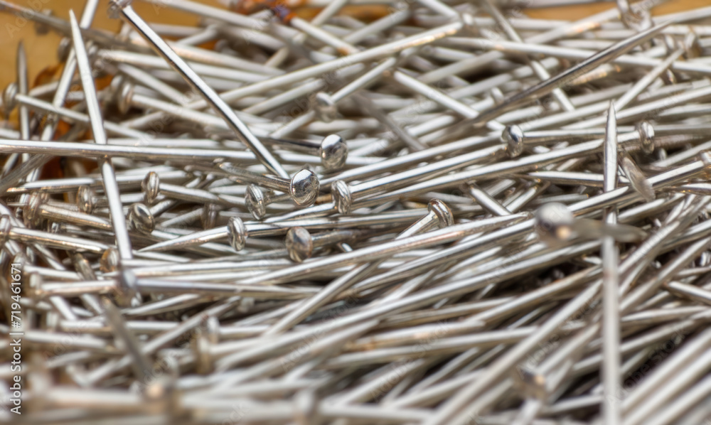 scattered pile of silver sewing pins on a wooden surface - fashion tailoring background selective focus