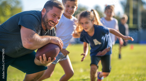 Elementary school coach playing American football with his students © JW Studio
